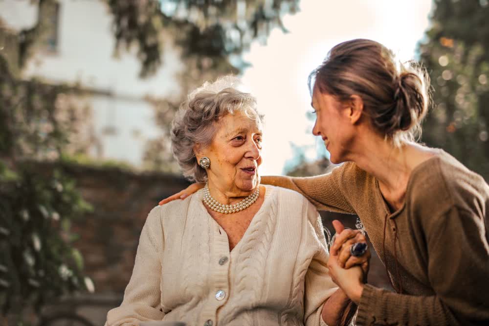 An adult daughter greeting her senior mother warmly in the garden